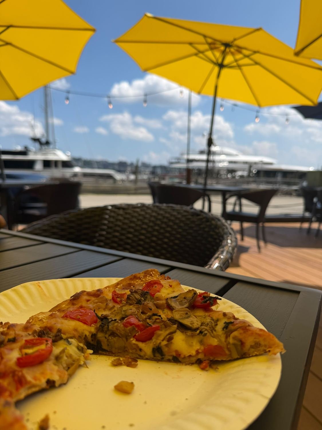 A table under a yellow umbrella on the terrace, with pizza and the marina behind